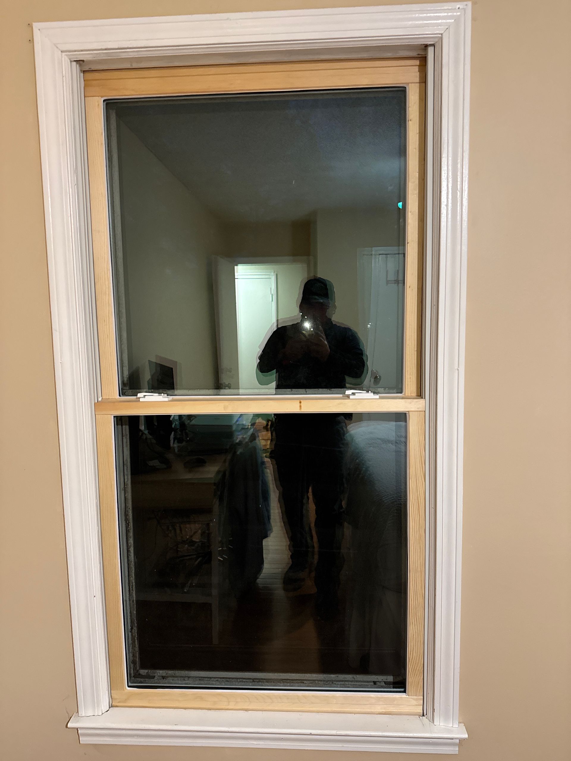 Interior window with white trim reflecting a person holding a phone in a dimly lit room
