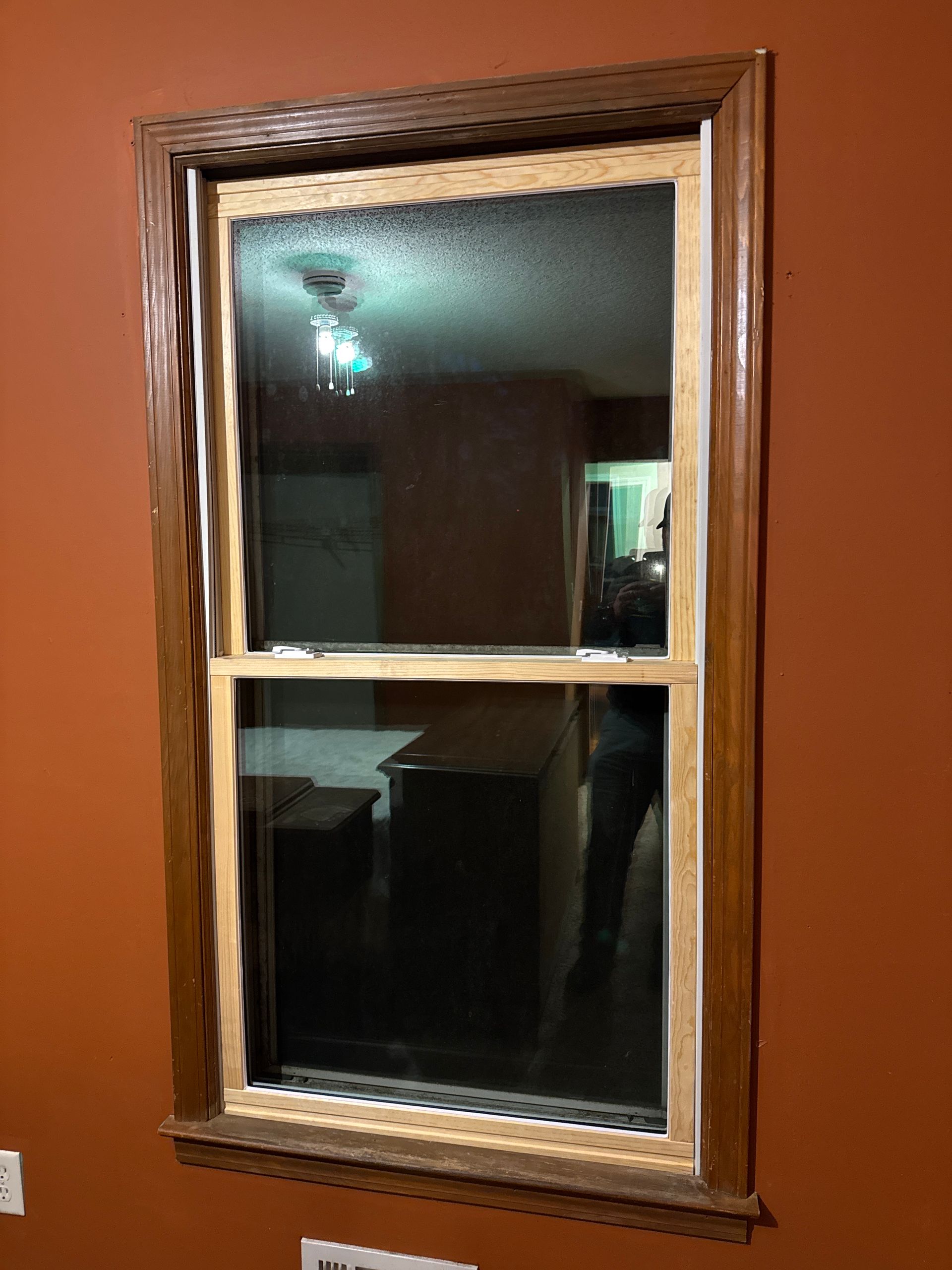 Wood-framed window in an orange wall, reflecting a dim interior room.