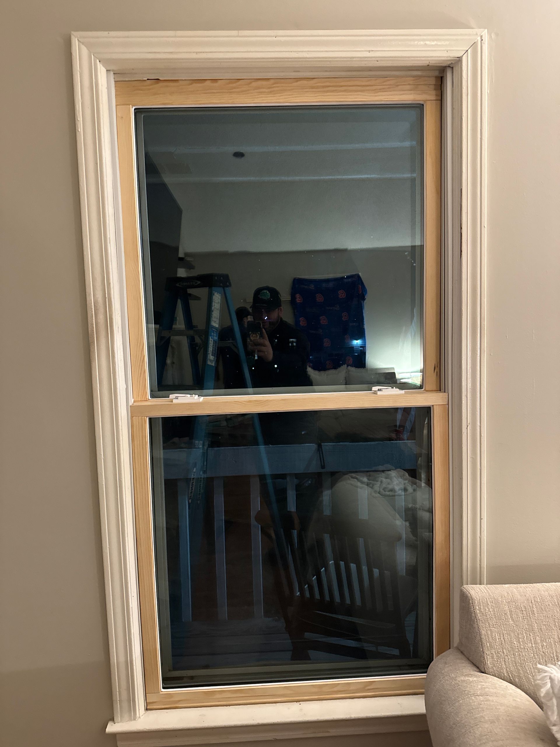Wood-framed window with two panes, reflecting an indoor room with chairs and a guitar.