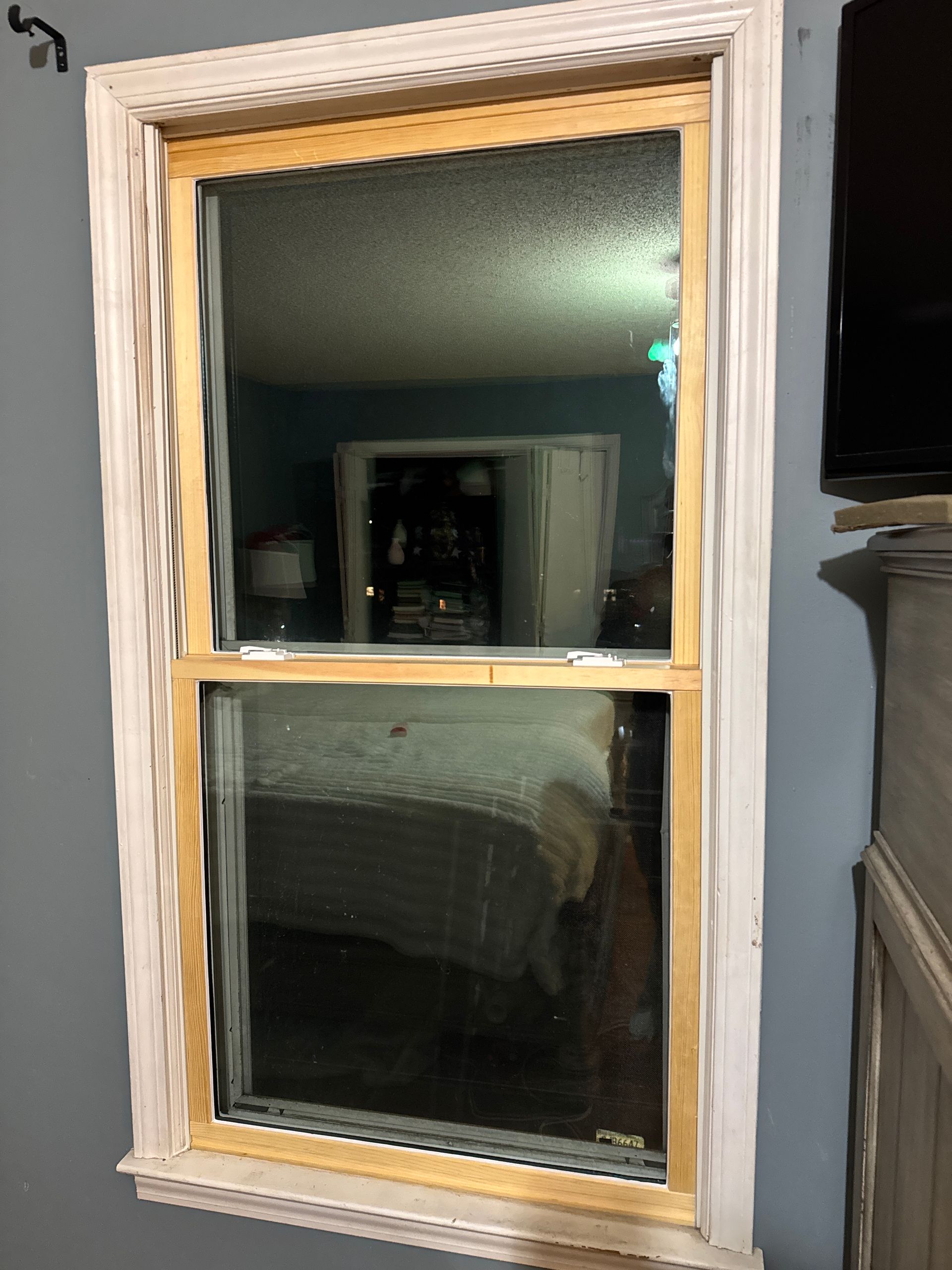 Single window with white trim on a gray wall, reflecting a dimly lit interior room.