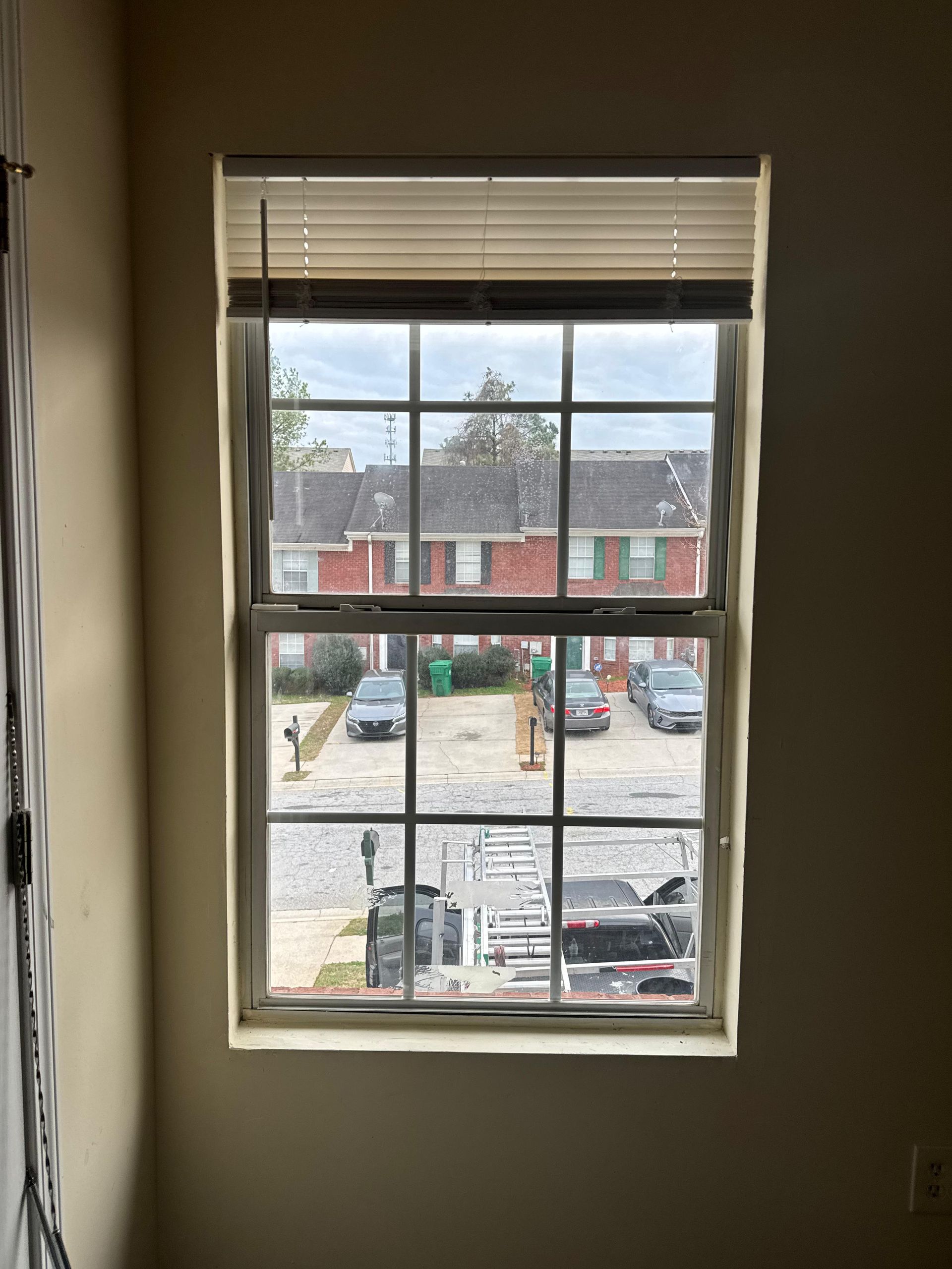 View through a window to a snowy apartment parking lot and red brick buildings.
