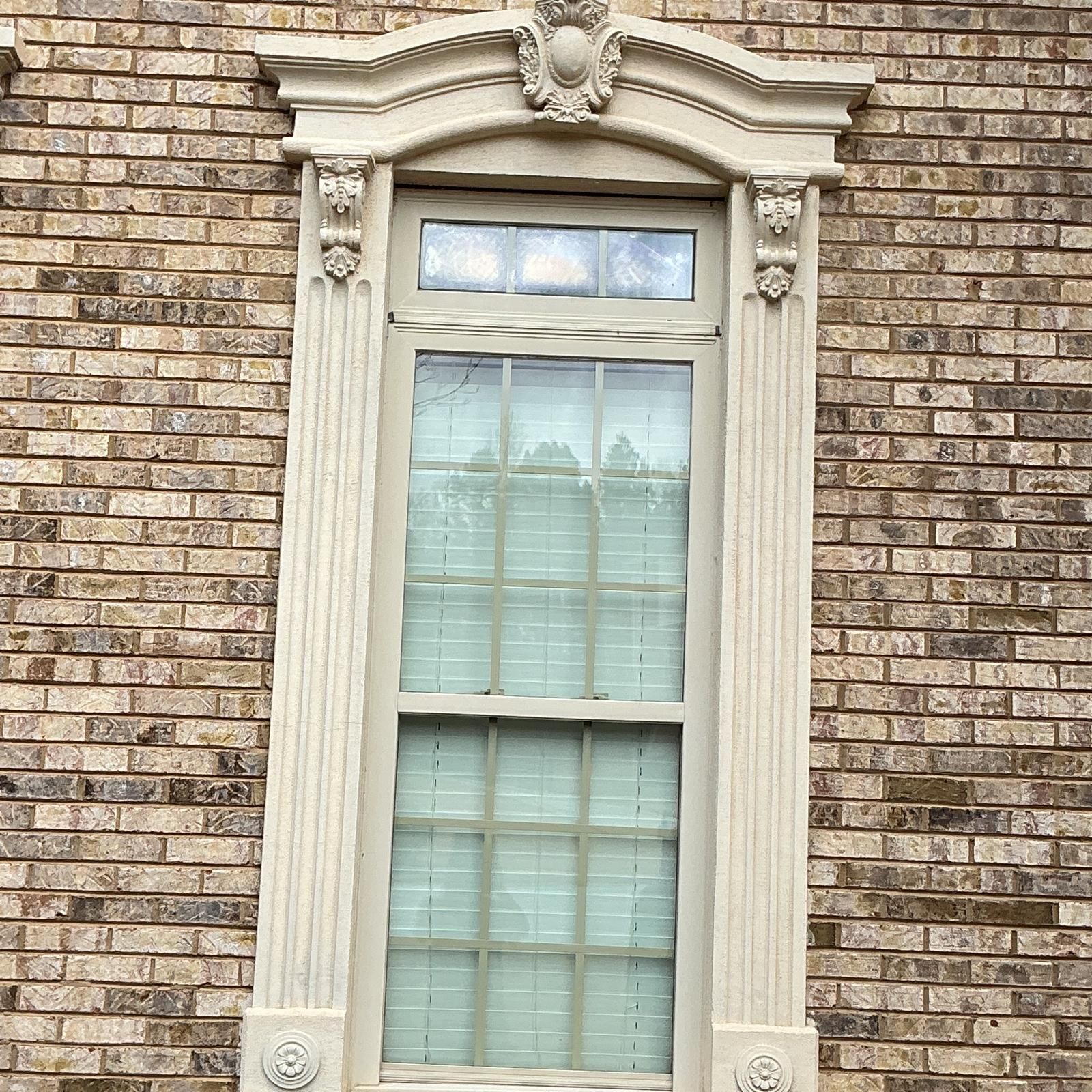 Ornate white-trimmed window set in a brown brick wall