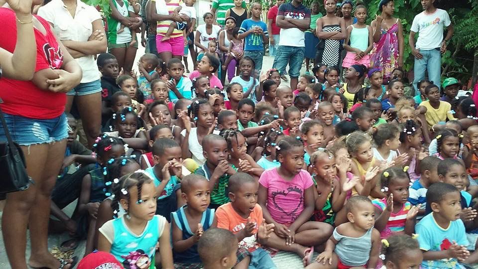 Crowd of children seated outdoors, gathered closely together with adults standing behind them