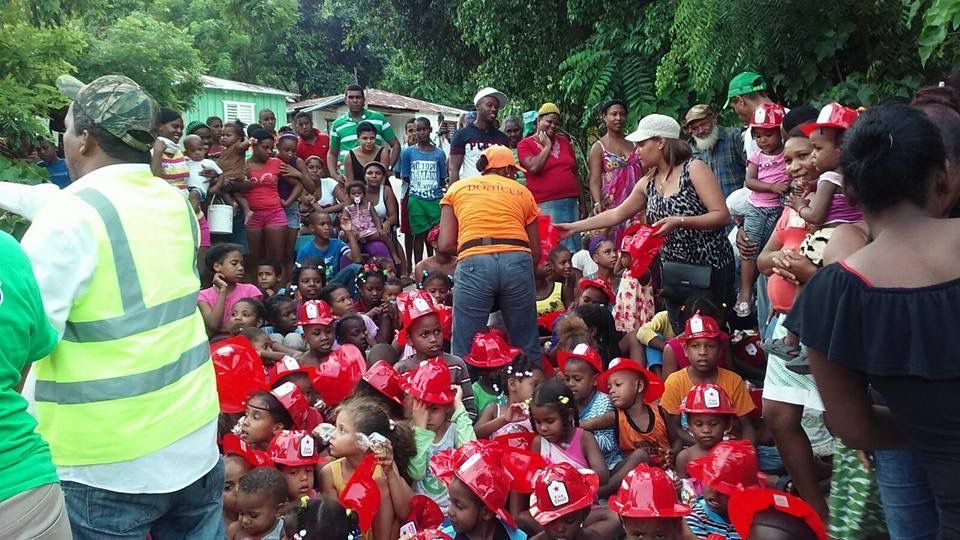 Crowd of people in red shirts gathered outdoors, with a volunteer in a reflective vest at left.