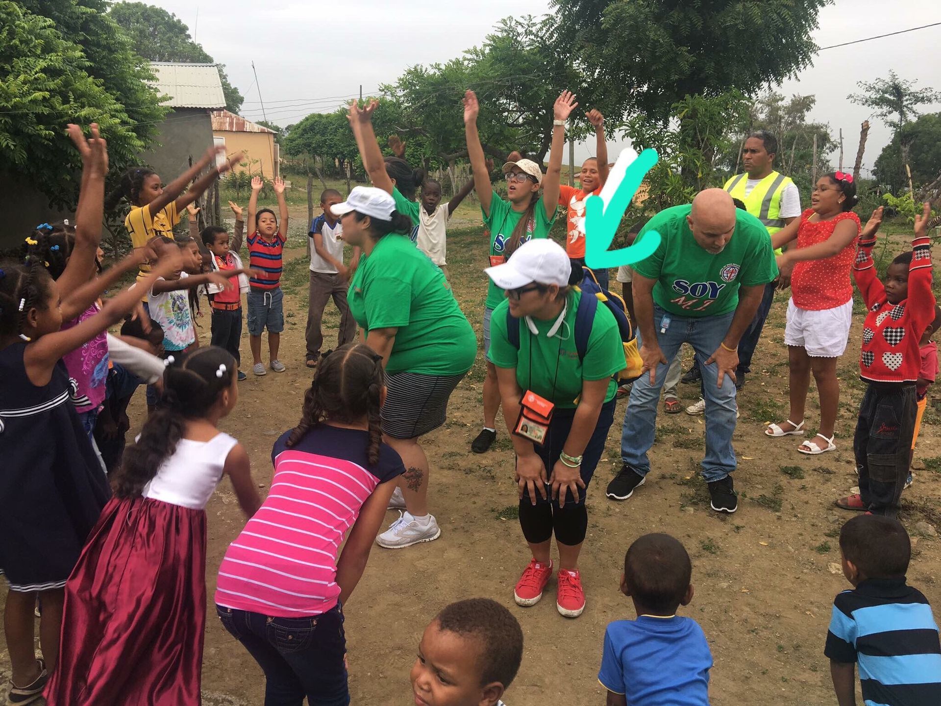 People dancing outdoors at a community gathering, with children watching and arms raised in celebration.