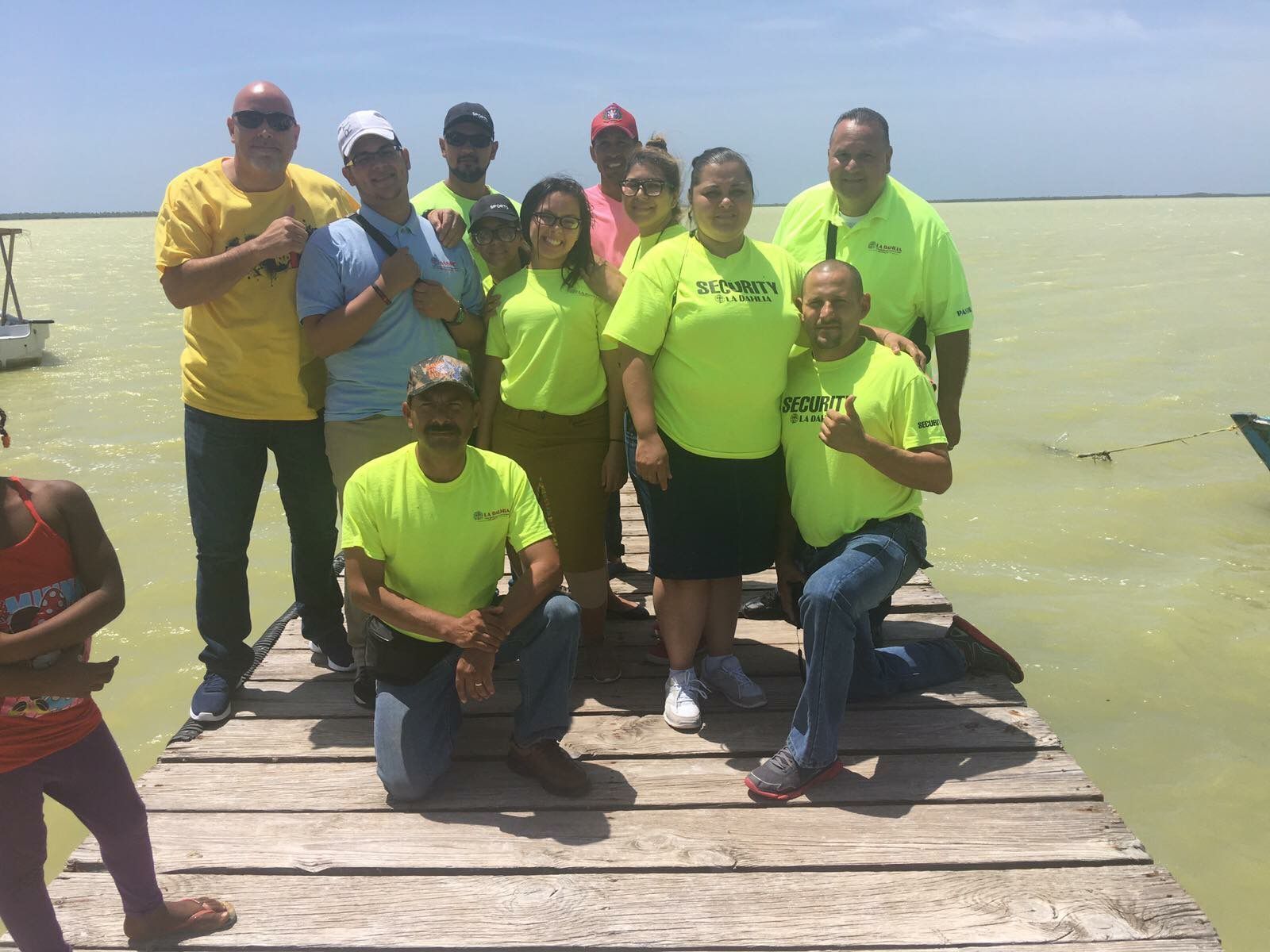 Group of people in bright shirts posing on a wooden dock by calm water under a clear sky
