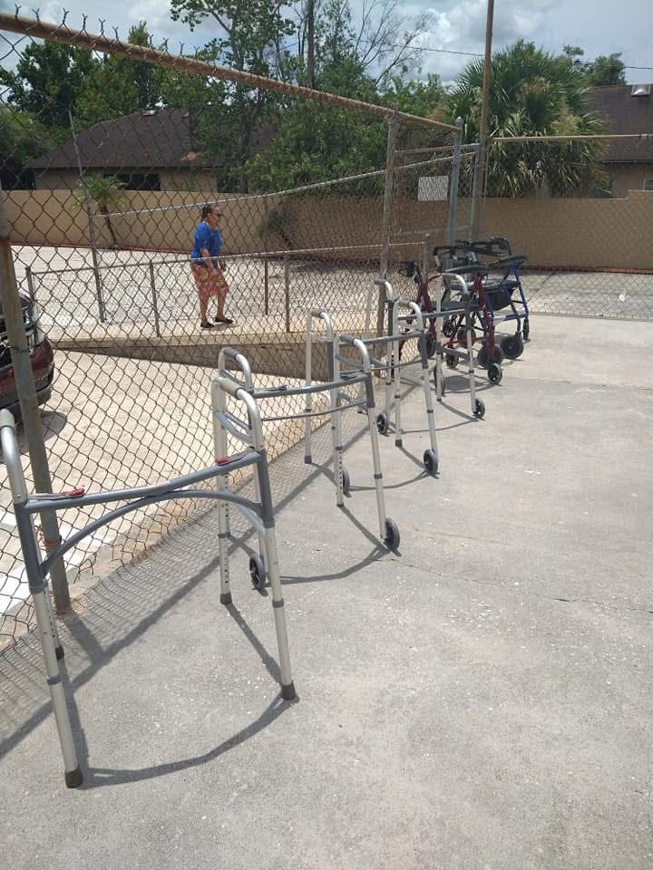 Folded metal tables beside a chain-link fence on a sunlit outdoor court, with a person in blue in the background