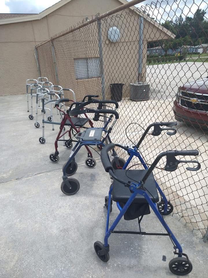 Blue and black walkers lined up on a concrete walkway beside a chain-link fence and tan building.