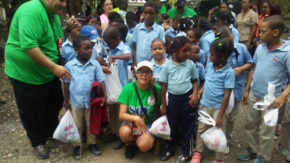 Children in blue uniforms gather outdoors with adults holding white plastic bags.