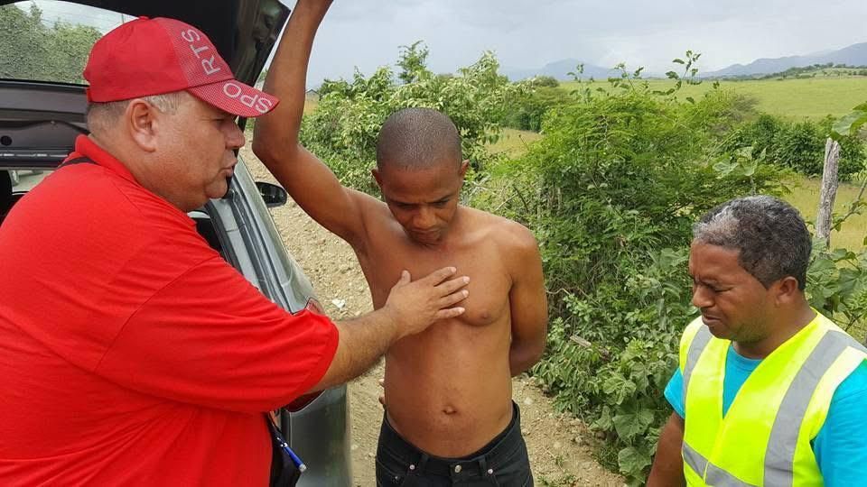Emergency workers assist shirtless man beside vehicle on rural roadside