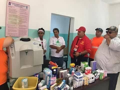People gathered around medical supplies and equipment in a clinical room, with boxes and bottles arranged on a table.