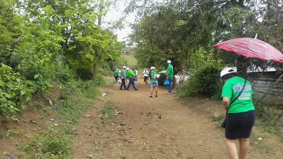 Hikers in green shirts walking along a muddy forest trail under cloudy skies, one carrying a red umbrella