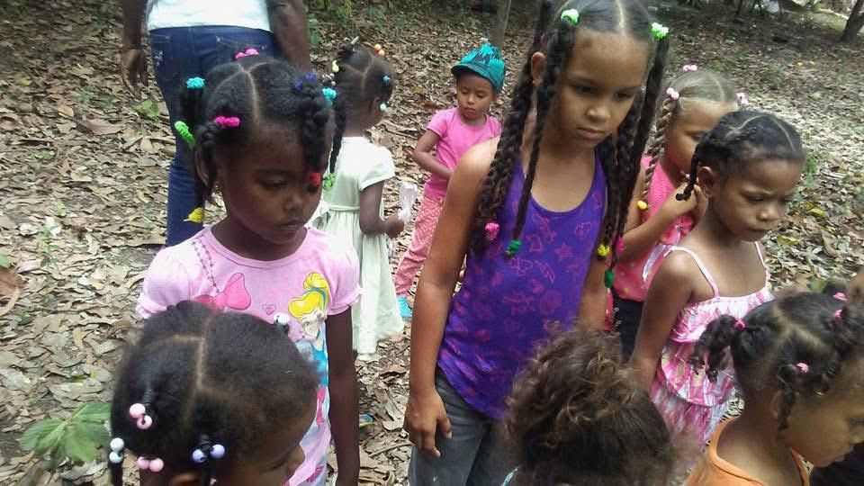 Children standing together on a rocky path in a wooded area, wearing colorful clothes and beads.