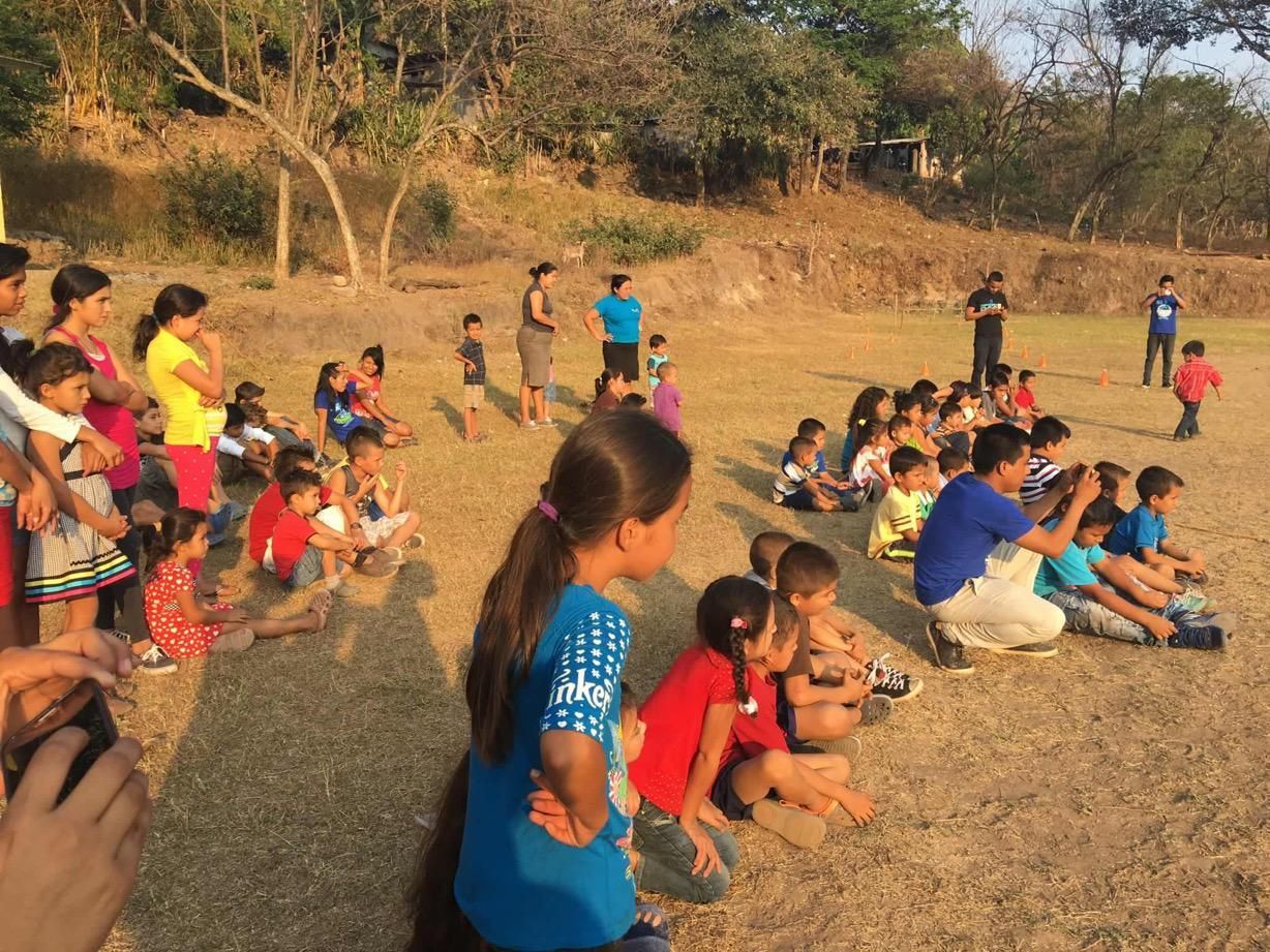 People gathered outdoors on a dry hillside, sitting and standing in a group during a community activity.