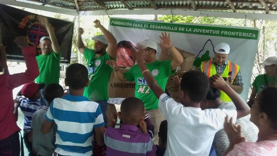People raising hands and singing on a stage with a green banner behind them