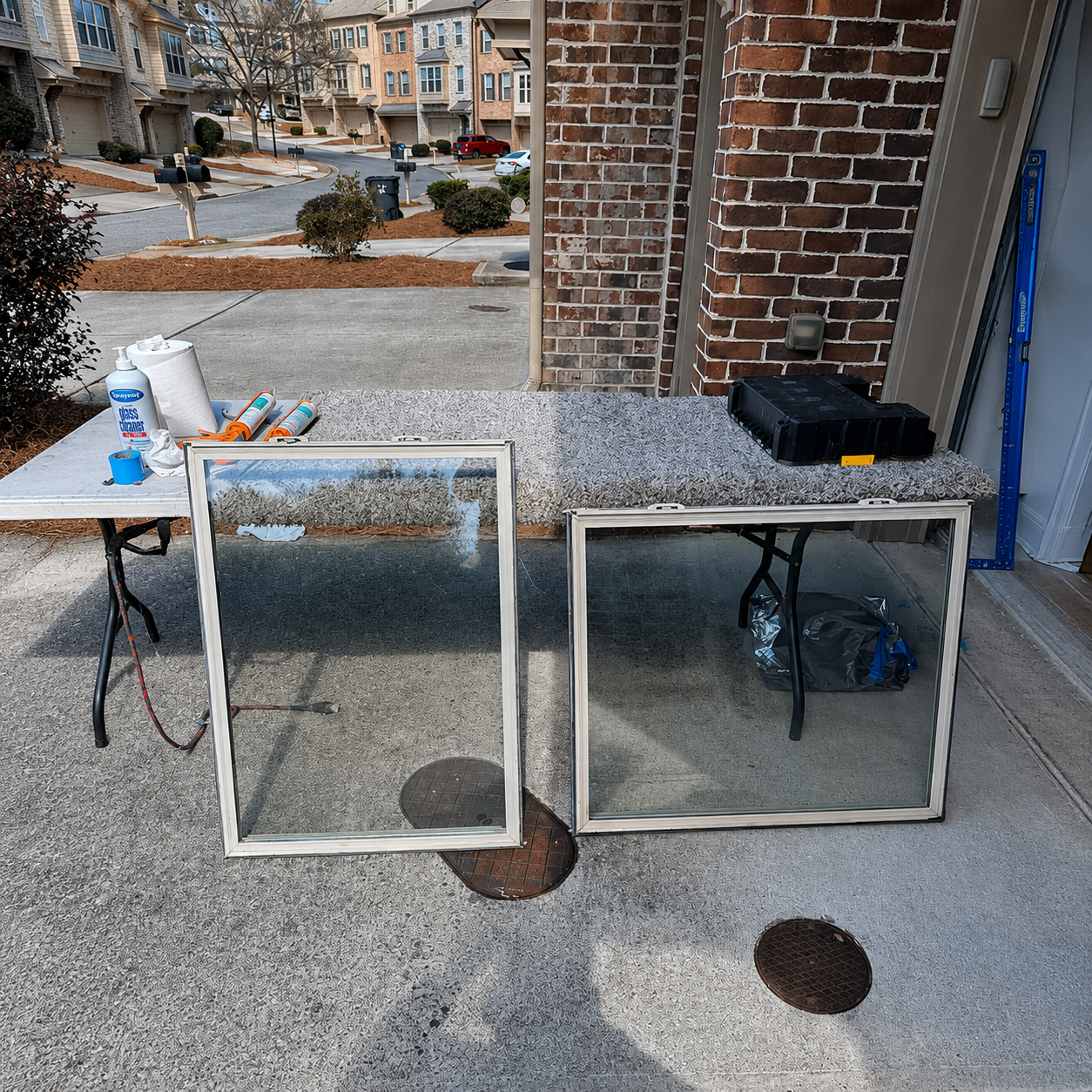 Two window screens leaning against a granite table on a driveway beside a brick house.
