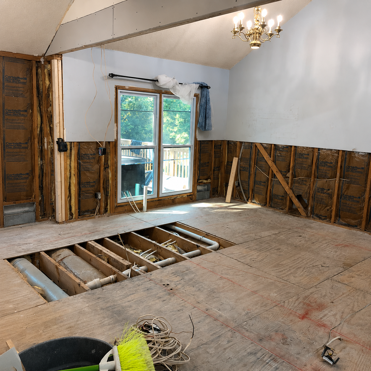 Partially demolished room with exposed floor joists, torn walls, and a sliding glass door to a deck.