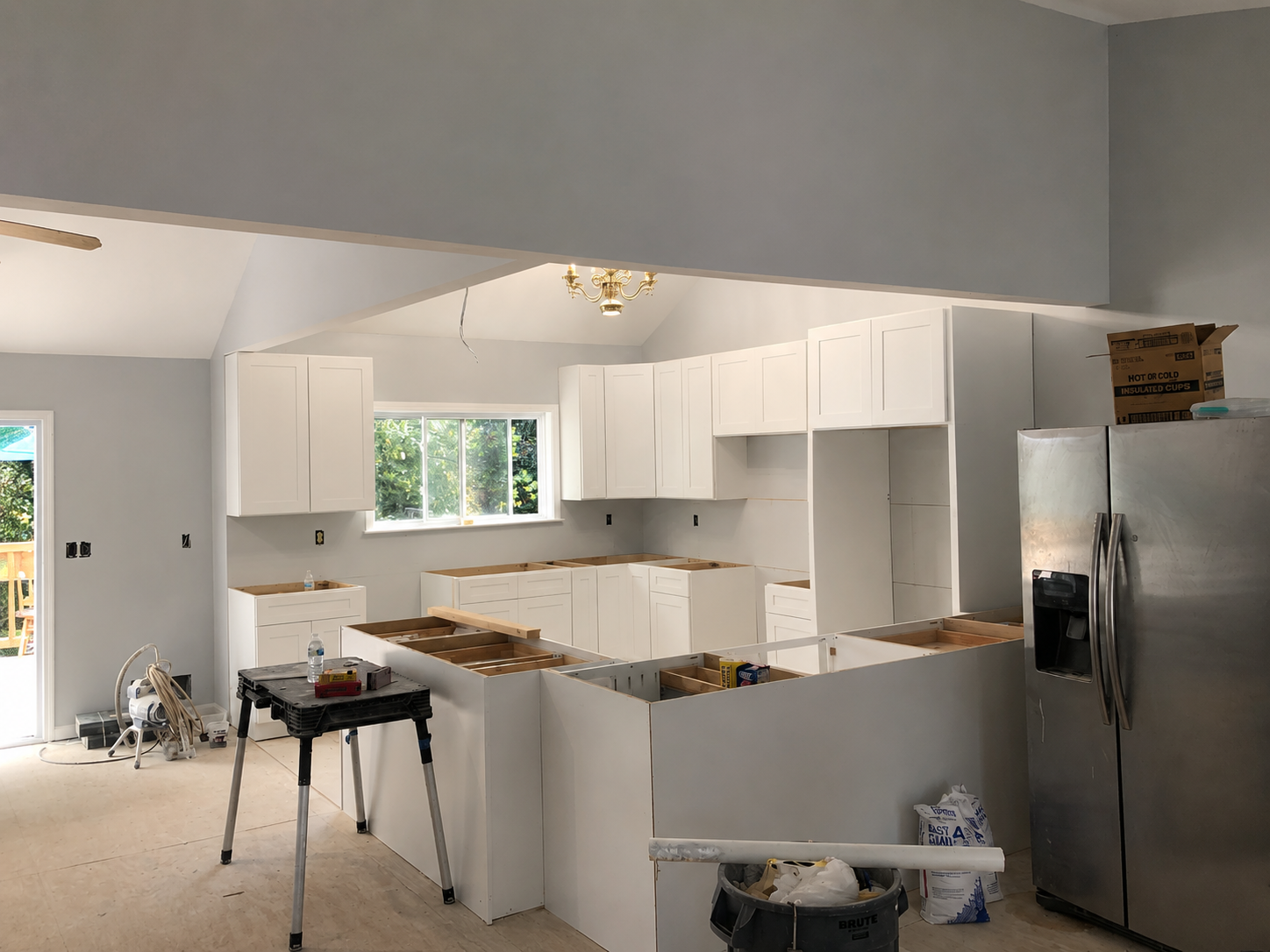 Kitchen renovation in progress with white cabinets, stainless refrigerator, and construction tools on the counter.
