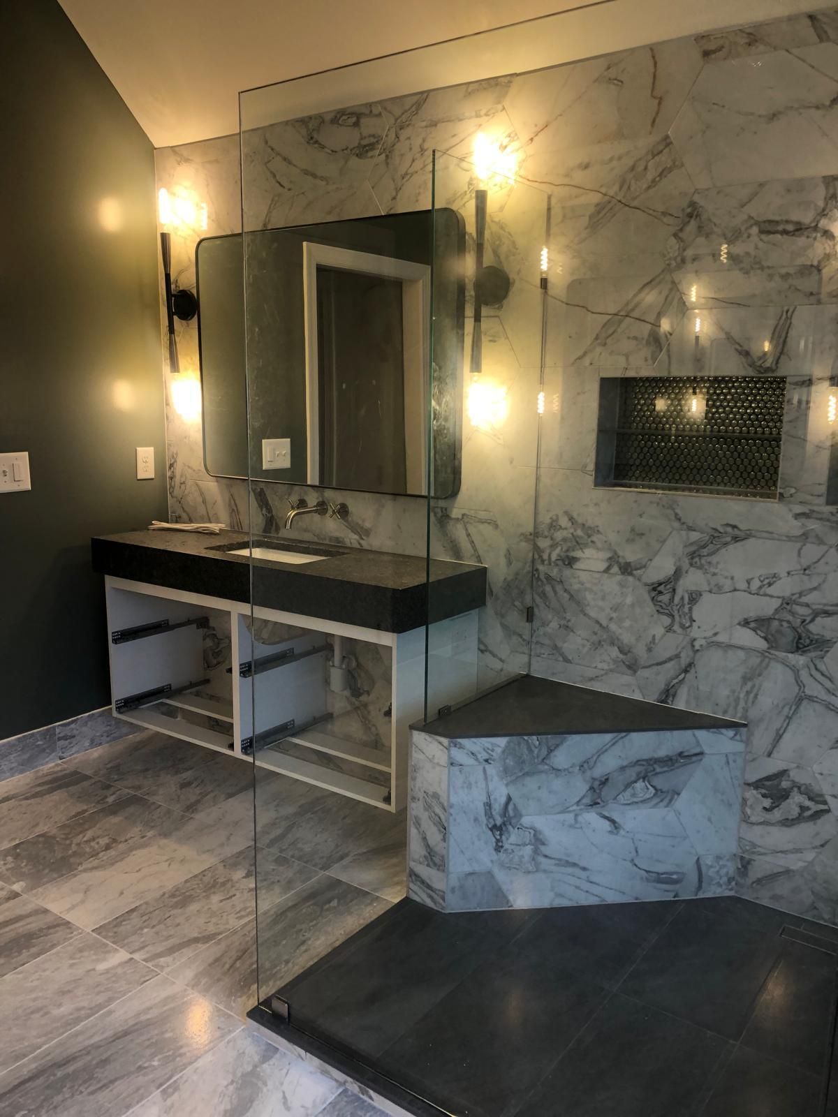 Marble-tiled bathroom with vanity, mirror, wall sconces, and tiled shower bench