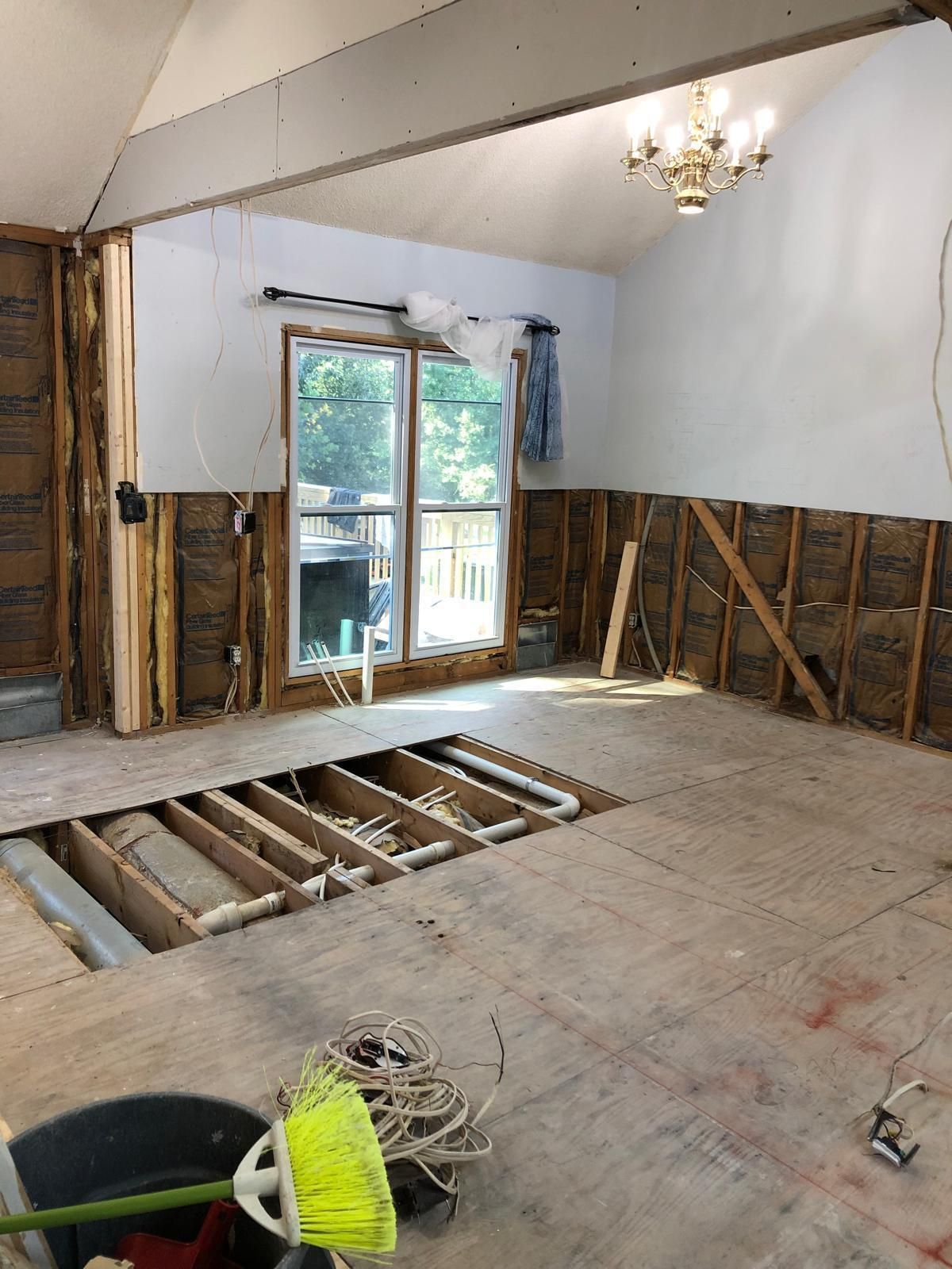 Partially renovated room with exposed floor joists, bare walls, and sliding glass door to a balcony.