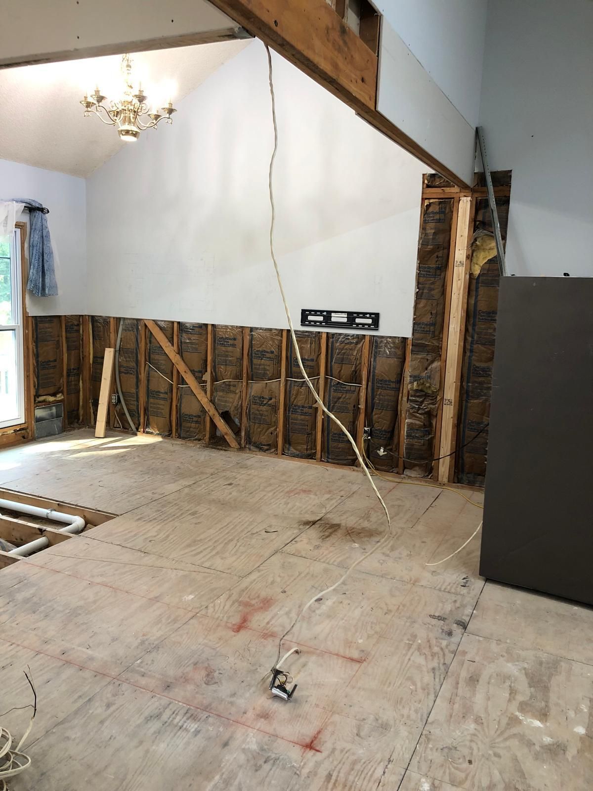 Partially renovated room with exposed wall studs, a sloped ceiling beam, and a chandelier hanging above.