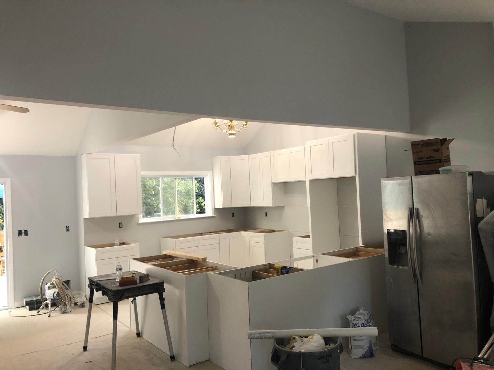 Kitchen under renovation with white cabinets, unfinished counters, and a stainless steel refrigerator