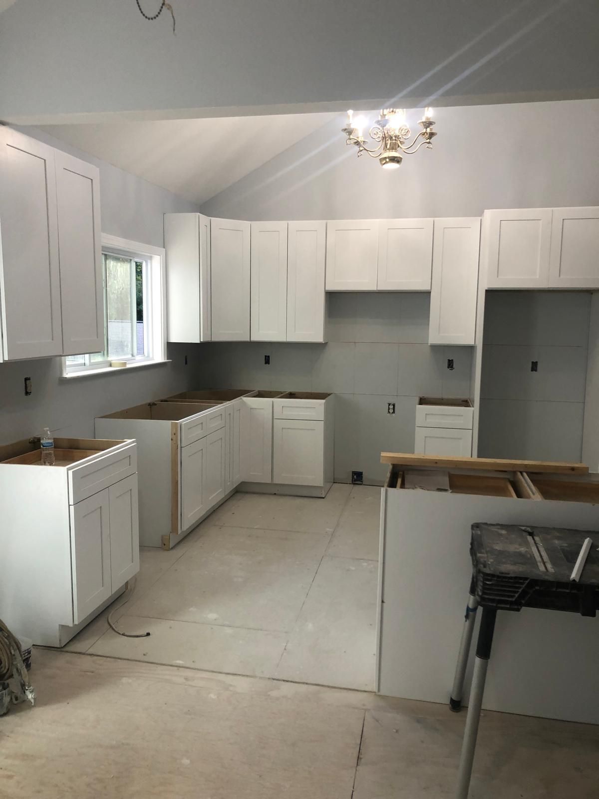 Partially renovated white kitchen with unfinished floor, cabinets, and appliances in place