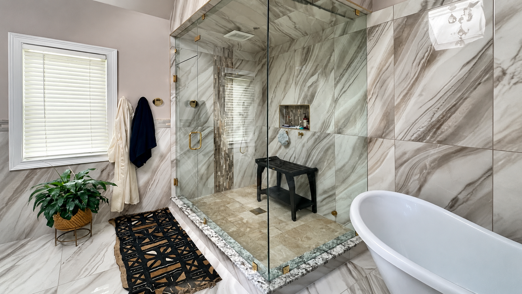 Marble-tiled bathroom with glass shower, black bench, potted plant, window, and freestanding tub