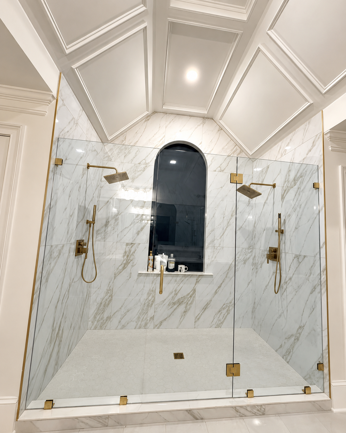 Marble-tiled walk-in shower with glass enclosure, gold fixtures, and an arched window.