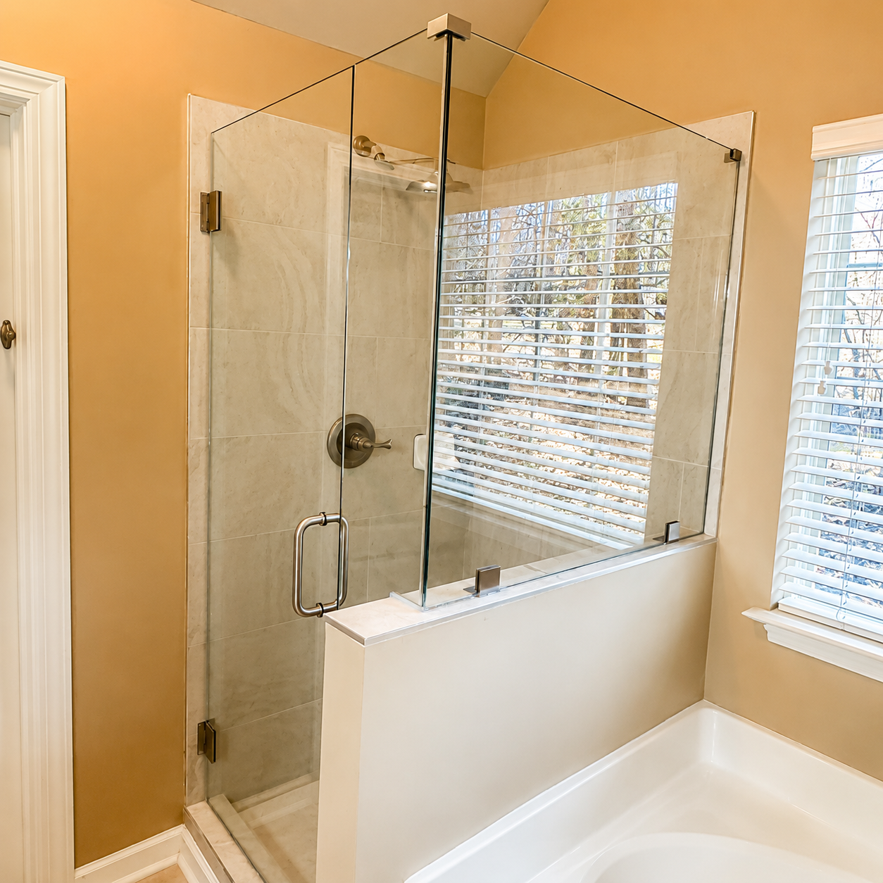 Bright marble bathroom with glass shower, freestanding tub, and large window