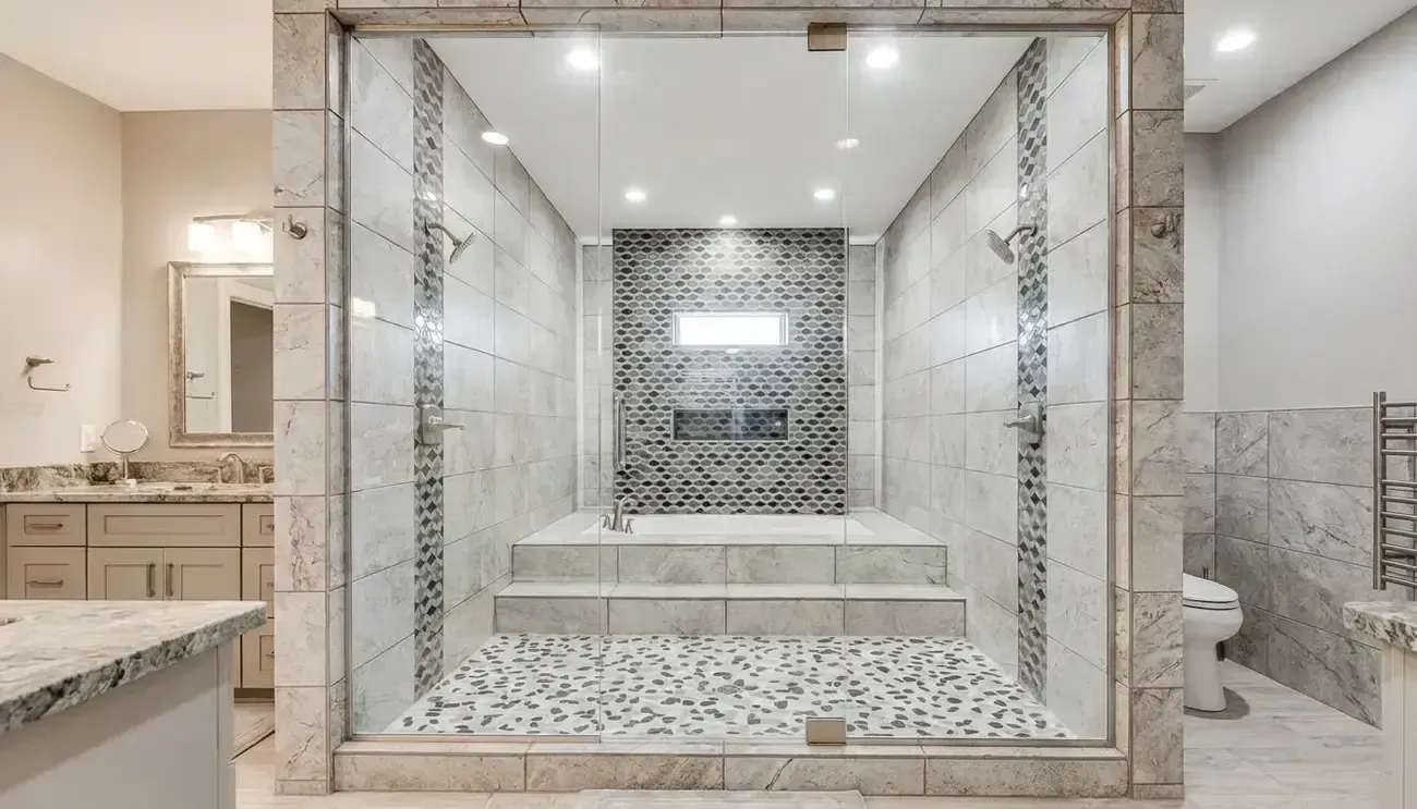 Luxurious marble-tiled shower with dual glass doors and steps in a bright bathroom