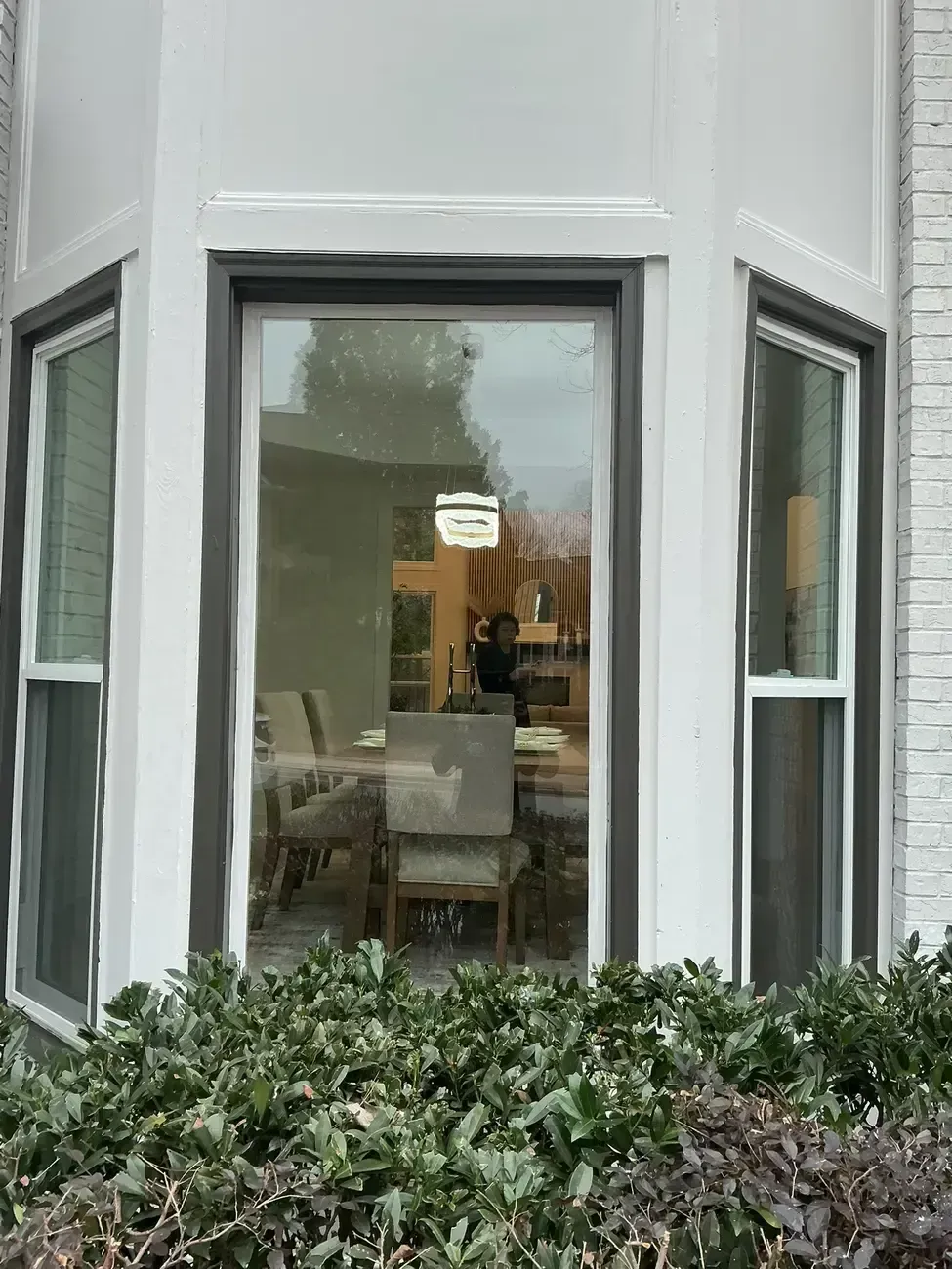 Bay window with white trim overlooking a dining area, partly obscured by shrubs outside