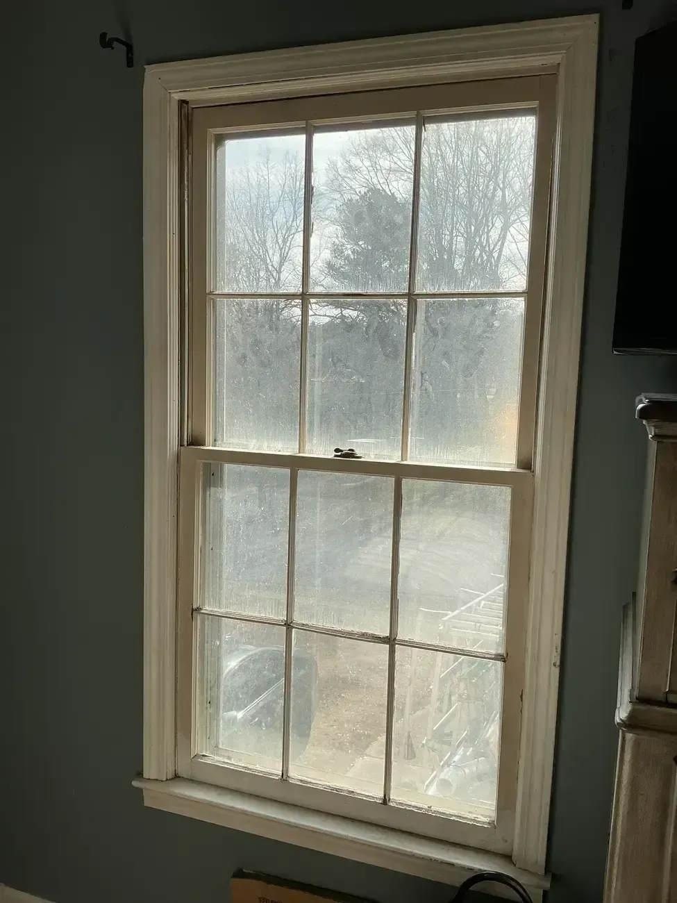 Dusty double-hung window with sunlight filtering through, set in a dim interior room.