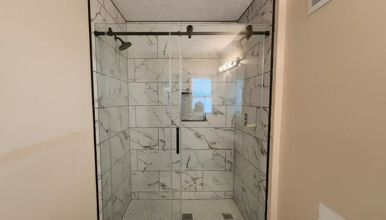 Frameless glass shower with marble-pattern tile and black hardware in a bathroom entrance