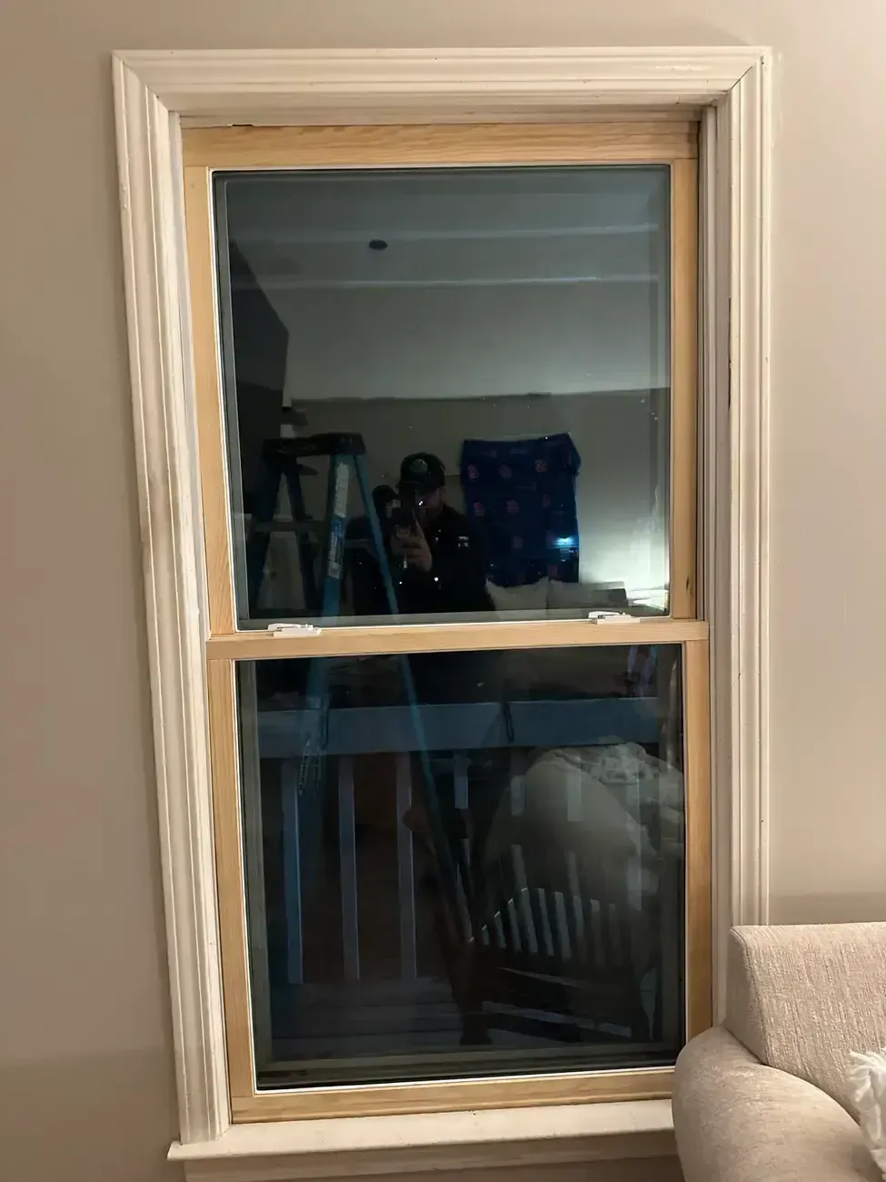 Window with white trim reflecting a room interior, including chairs and a table.