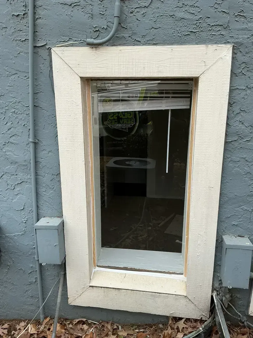 Small basement window with white trim set in a blue-gray exterior wall.