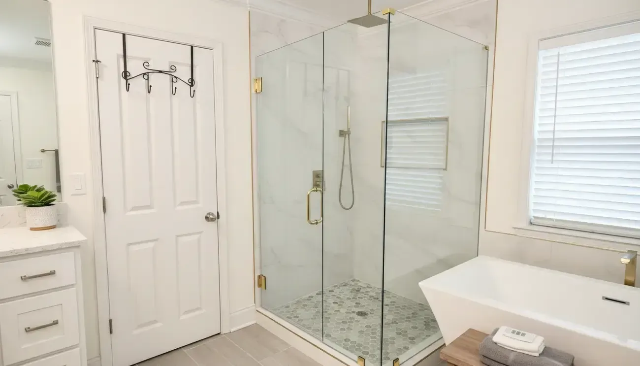 Bright white bathroom with glass shower, double vanity, and white tub under window blinds