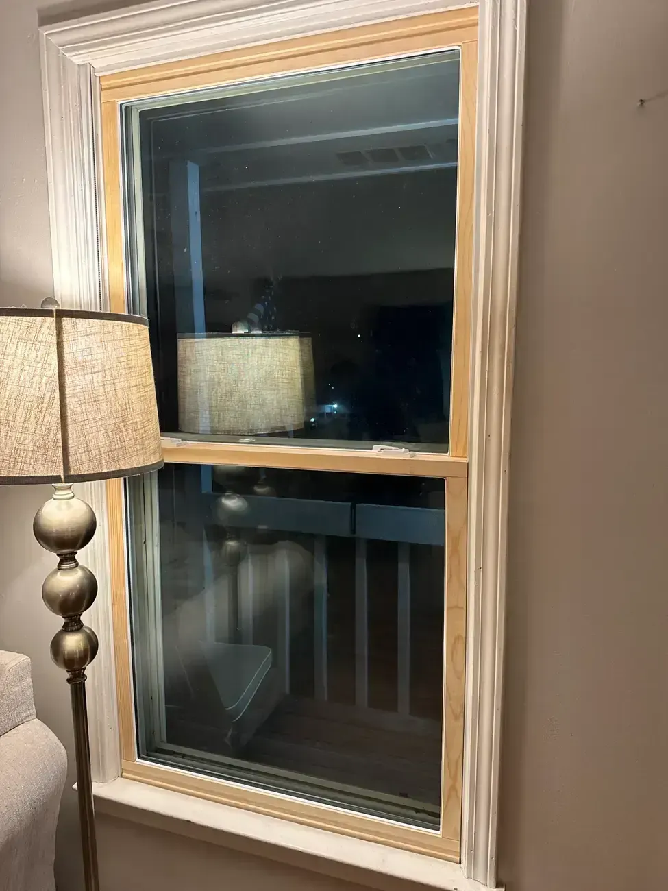 Living room window at night with beige trim, lamp reflection, and a floor lamp beside it