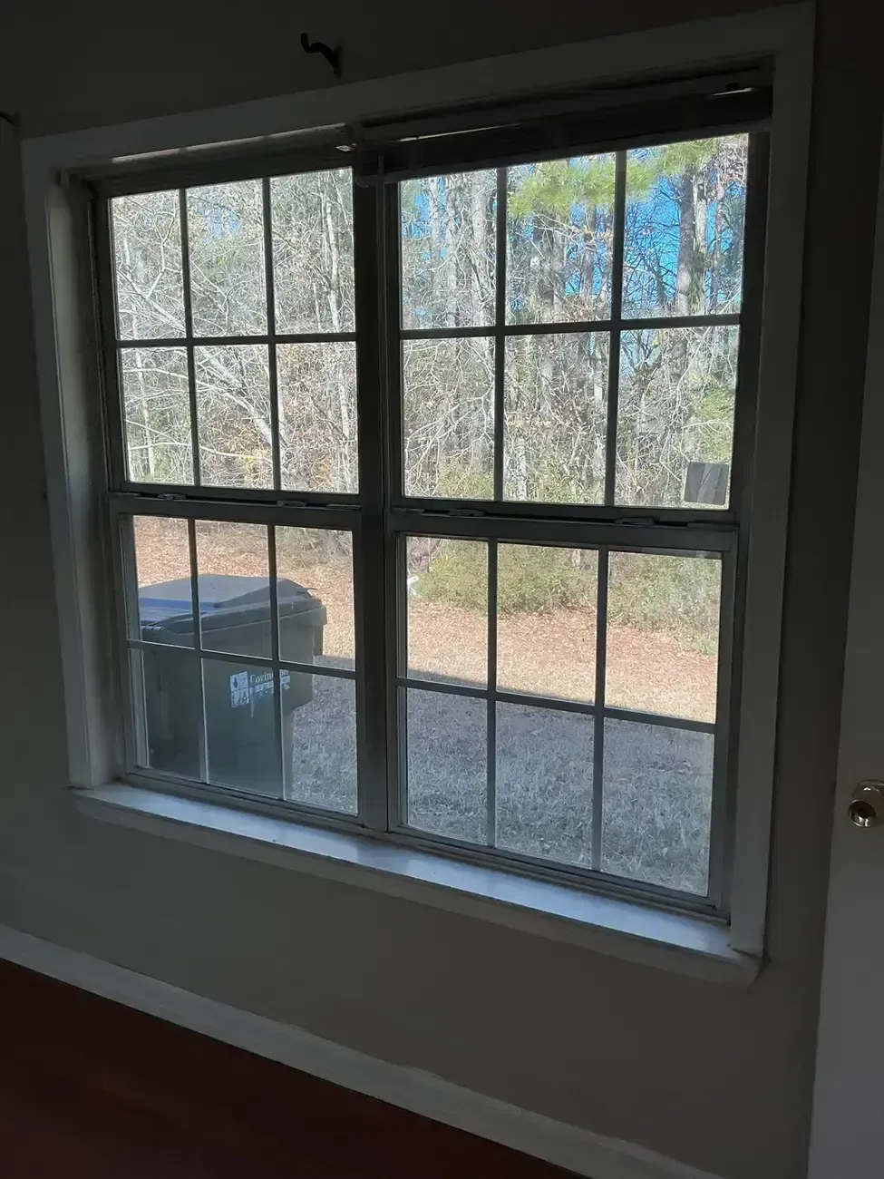 Sunlit window with white trim overlooking a fenced yard and gravel patio