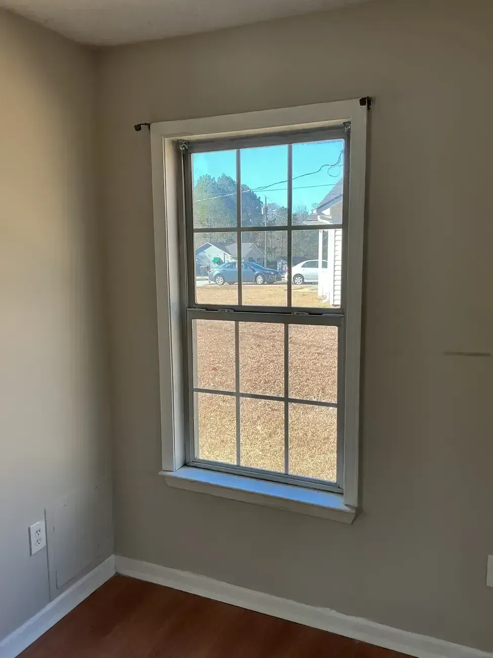 Empty beige room with a single window showing a yard and trees outside