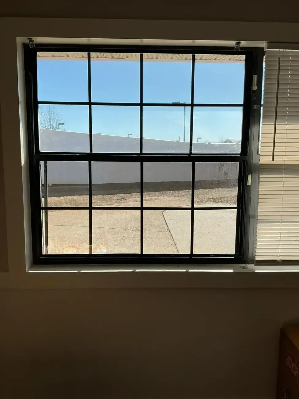 Window with black grid panes overlooking a sunlit desert landscape and blue sky