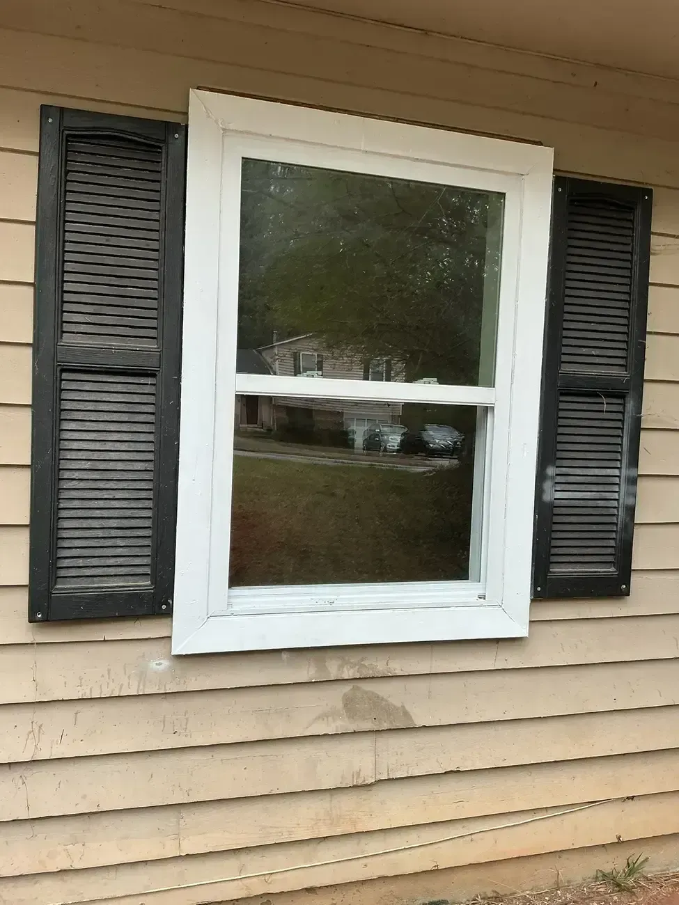 House window with white frame and black shutters on beige siding