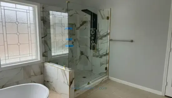Bright bathroom with marble-tiled tub, glass shower, window, and white walls