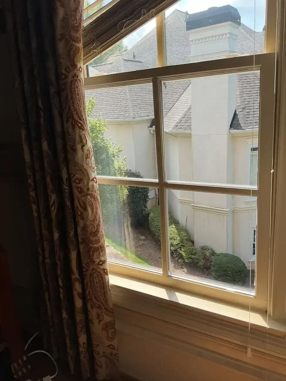 Sunlit window with curtains, looking out to a backyard and white fence