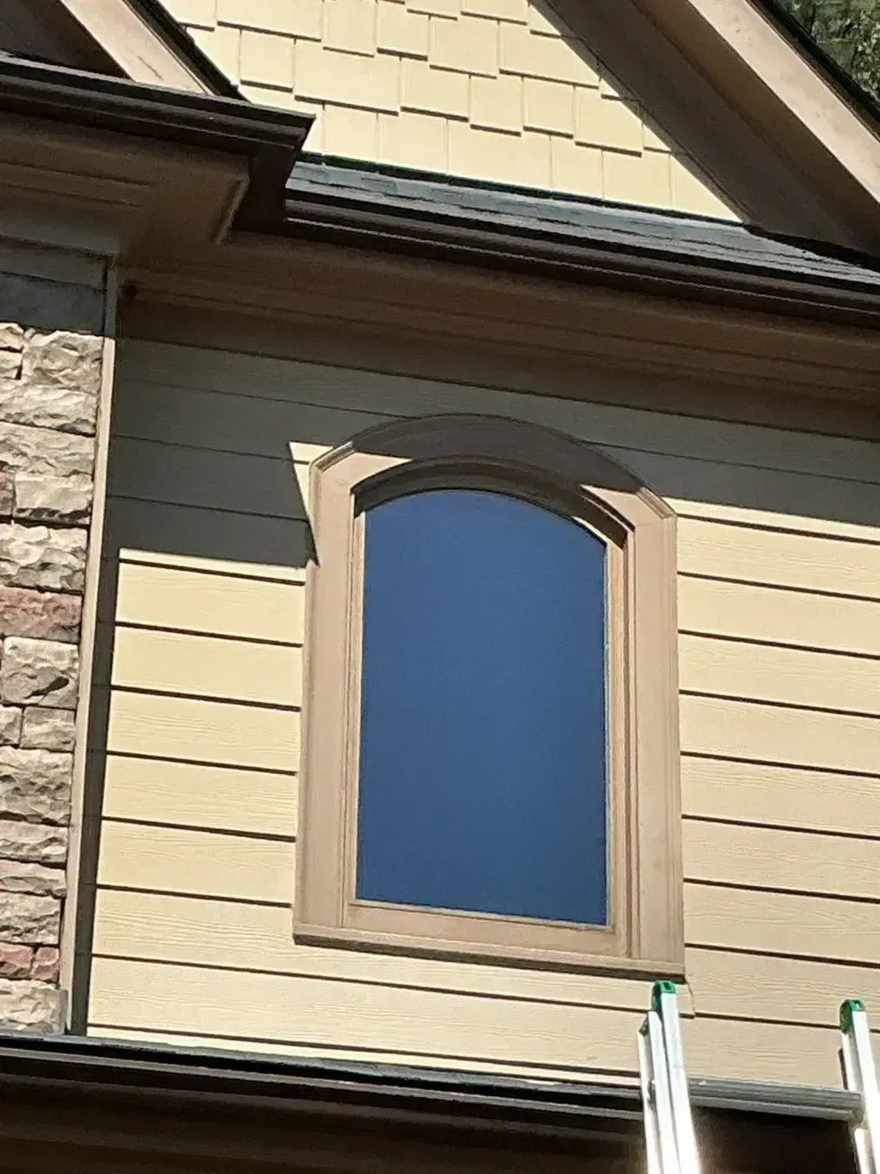 Arched window on beige siding beside stone exterior wall and roof eave