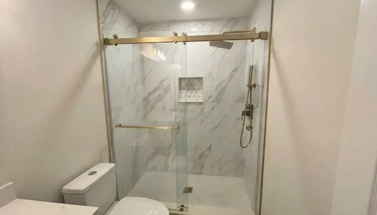 Modern bathroom shower with marble-look tile, glass door, and toilet beside it