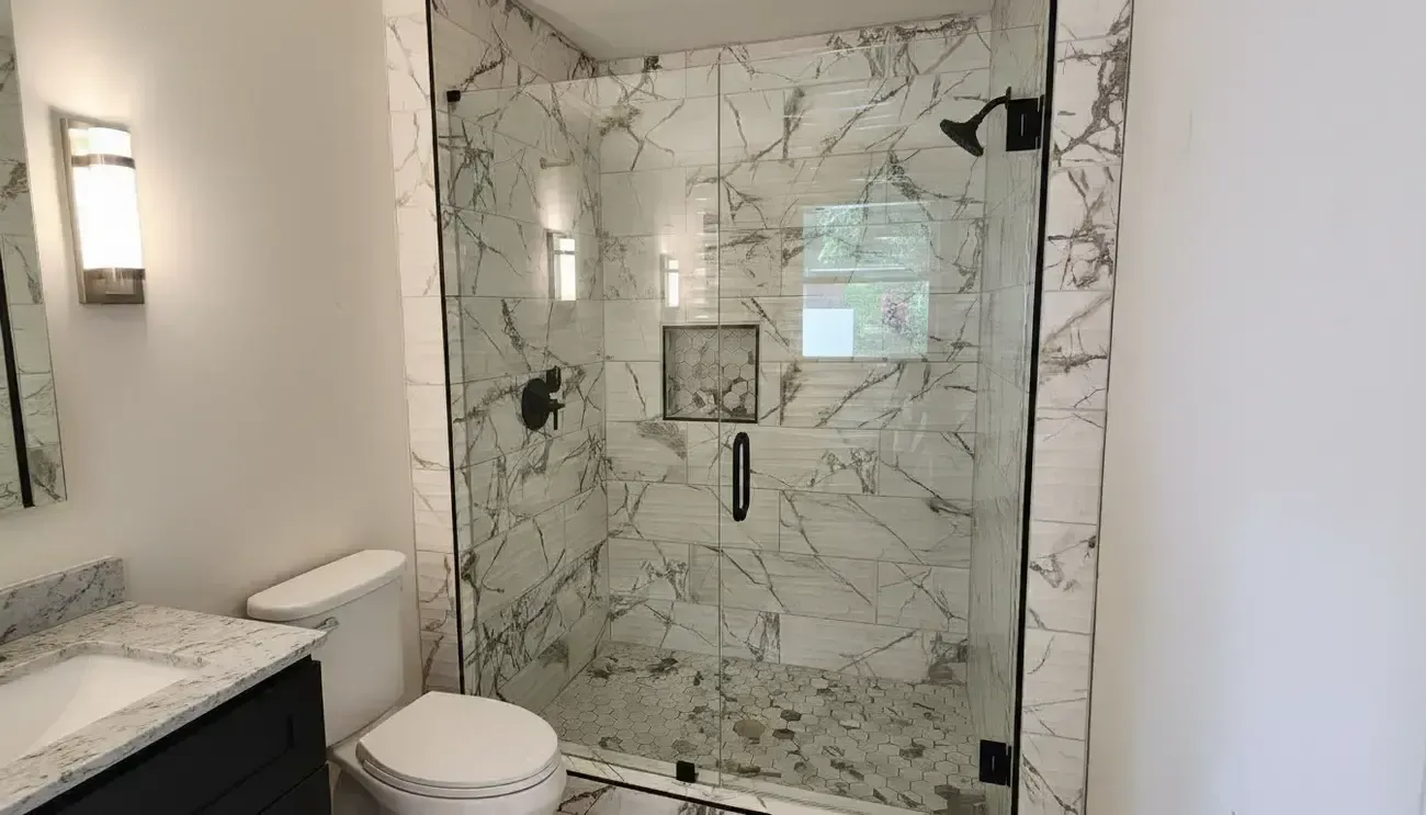 Modern bathroom with marble shower, glass door, vanity sink, toilet, and wall sconce