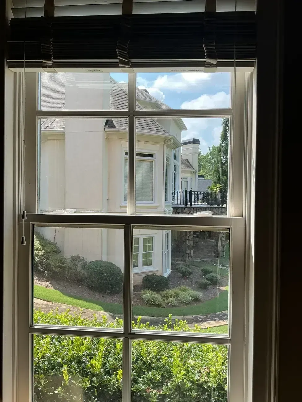 View through a window of a white house and landscaped garden with shrubs and trees outside