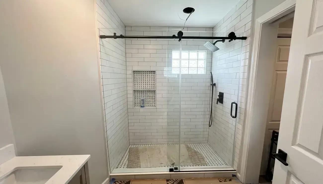 Bright white tiled walk-in shower with glass enclosure and black hardware in a bathroom