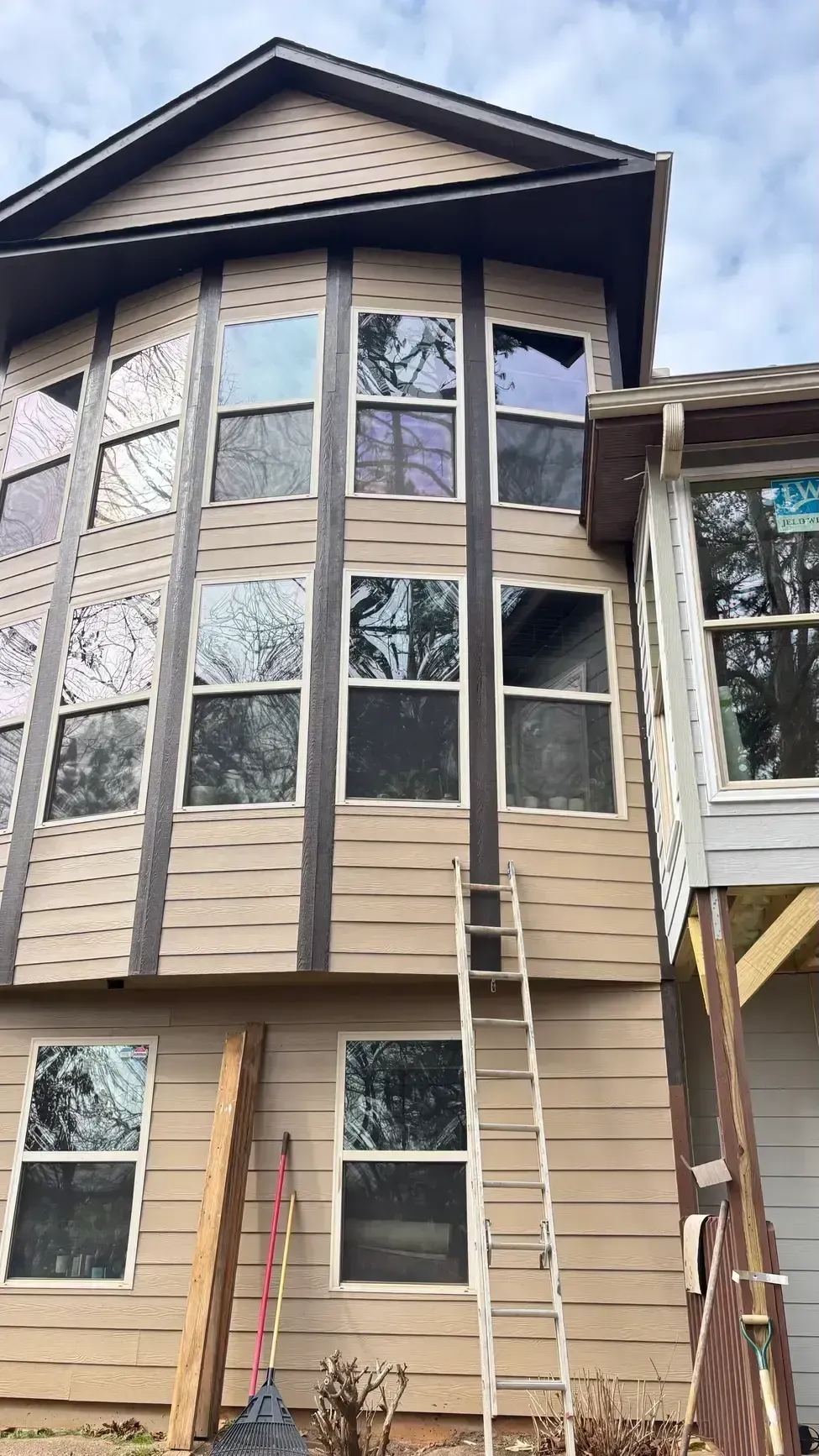 Tall beige house with large windows and two ladders leaning against the front.